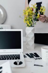 Woman, yellow flowers in a vase, white laptop, cup, desk
