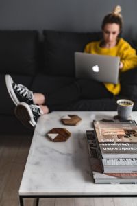 Woman with legs on the coffee table, wearing converse sneakers and working on her laptop