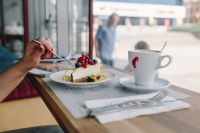 Woman Enjoying Cheese Cake and a Coffee with Fruits in a Cafeteria