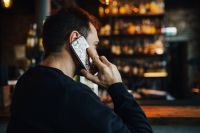 Handsome young man with smartphone drinking whisky at bar or pub