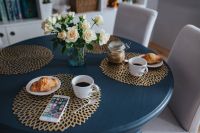 Round breakfast table with white flowers, golden mats, coffee, croissant and smartphone