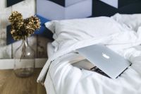 An ornamental golden plant in a jar by the bed with white sheets and a laptop