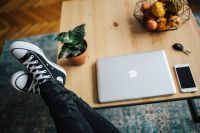 Woman in ripped jeans and black sneakers with a silver laptop on a wooden table