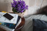 Books, purple flowers and a white smarphone on a wooden stool by the bed
