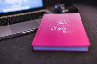 Pink notebook with a silver laptop and a camera