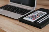 Silver Acer laptop, a white Apple iPhone and a black notebook on a wooden desk