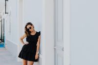 Kaboompics - A young woman with dark hair wearing a black dress poses by the blue building
