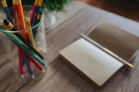 Small notebooks with colourful pencils in a jar on a wooden desk
