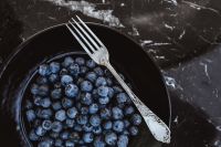 Fresh blueberries on a black plate with vintage cutlery