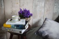 Books, purple flowers and a white cup on a wooden stool by the bed