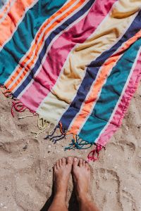 Womans' feet and colorful beach towel on the sand
