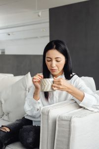 A young Asian woman relaxes on the couch and drinks coffee or tea