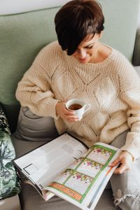 Kaboompics - The woman is drinking tea on the couch and reading the newspaper
