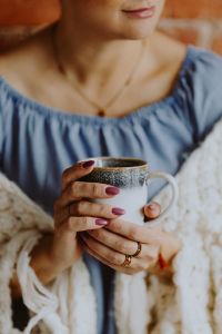 Kaboompics - A woman in a warm blanket holds a cup of coffee or tea