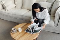A young Asian woman sits on the couch and reads a book or magazine