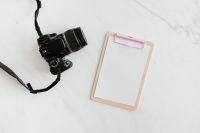 Kaboompics - Clipboard and camera on a marble table, copy space