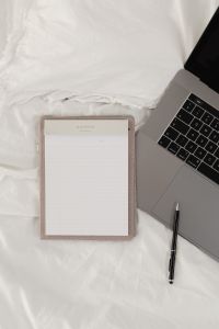 Working with a laptop in bed - white cotton bedding - blank notebook - pen