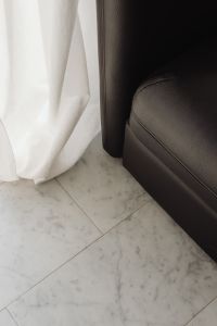 Detail of a black leather armchair with marble flooring and white curtains