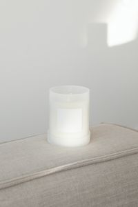 Candle in white glass with label on linen couch