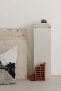 A variety of marble and stone materials - cut into abstract - geometric shapes - leaning against a wall in a minimalist display.