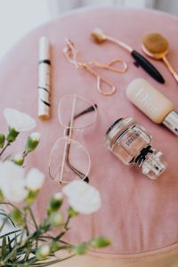 Makeup brushes, eyelash curler & a bottle of perfume on pink velvet