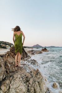 Kaboompics - A woman in a green dress on a rock by the sea