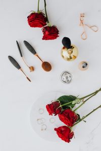 Red roses, gold jewellery and beauty accessories on white marble