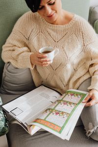 Kaboompics - The woman is drinking tea on the couch and reading the newspaper