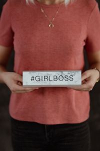 A young woman is holding a Girlboss Desk Sign