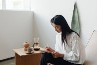 Asian adult sits in chair and writes in notebook - draws - table - coffee - Chemex - agave