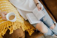 Kaboompics - Woman with a cup of coffee & book, yellow blanket, blue jeans pants
