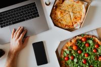 Top view of the desk with pizza, laptop, phone and hands