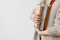 A young woman in a woolly sweater holds books