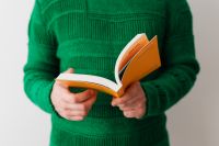 A man in a green sweater reading a book, white background