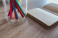 Kaboompics - Small notebooks with colourful pencils in a jar on a wooden desk
