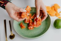 Kaboompics - A woman peels an orange on a green plate