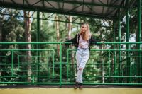 Kaboompics - Blonde woman in a black jacket and ripped jeans by a green handrail