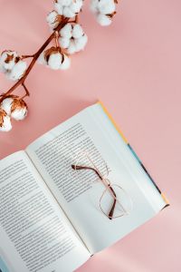 Kaboompics - An open book, glasses and a cotton branch on a pink background