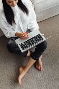 Adult young Asian woman sits in living room and works on laptop
