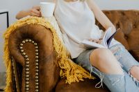 Woman with a cup of coffee & book, yellow blanket, blue jeans pants, brown couch