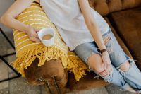 Woman with a cup of coffee & book, yellow blanket, blue jeans pants