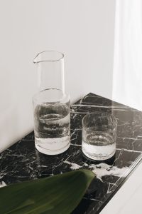 Water in a transparent glass carafe and glasses on a black marble console