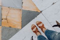 Kaboompics - A woman wearing blue jeans and leather sandals stands on a marble, natural stone floor