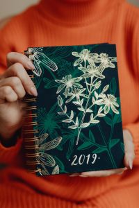 Kaboompics - A woman in an orange sweater holds the 2019 calendar in her hands