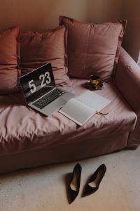 Workplace with a laptop, organizer, high heels shoes and coffee on a pink couch