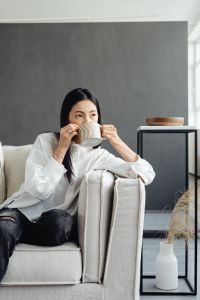 A young Asian woman relaxes on the couch and drinks coffee or tea