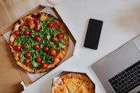 Top view of the desk with pizza, laptop, phone and hands