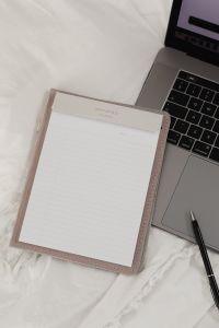 Working with a laptop in bed - white cotton bedding - blank notebook - pen