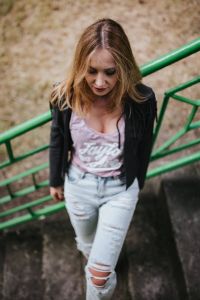 Blonde woman in a black jacket and ripped jeans by a green handrail