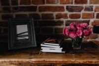 Photo frame, books and pink flowers in a vase on a wooden commode